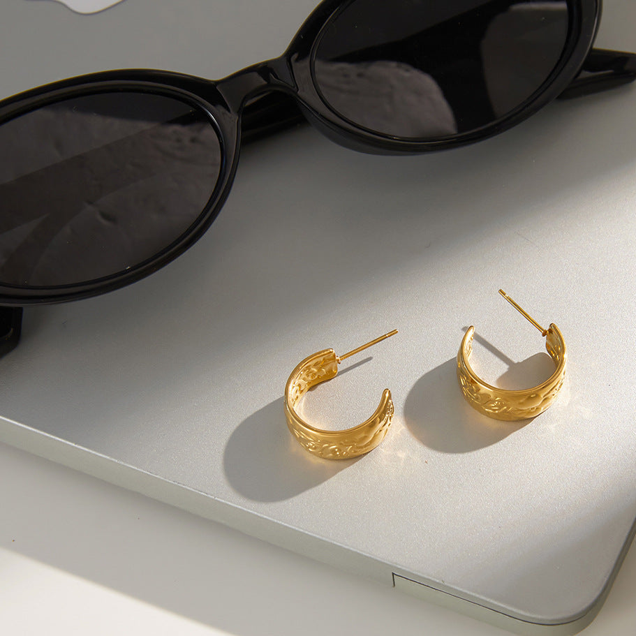 Gold hoop earrings on a white surface with sunglasses and a product packaging.