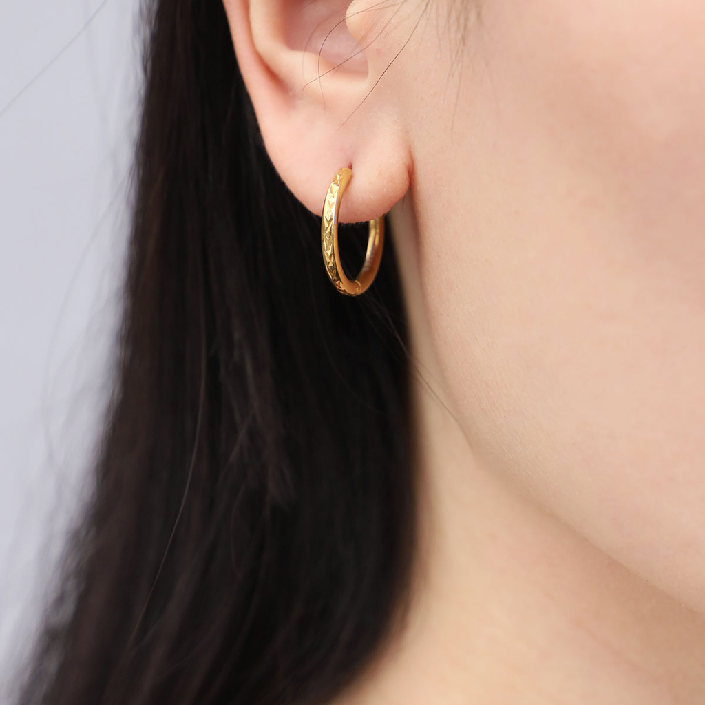 Gold hoop earring worn by a person with dark hair on a neutral background