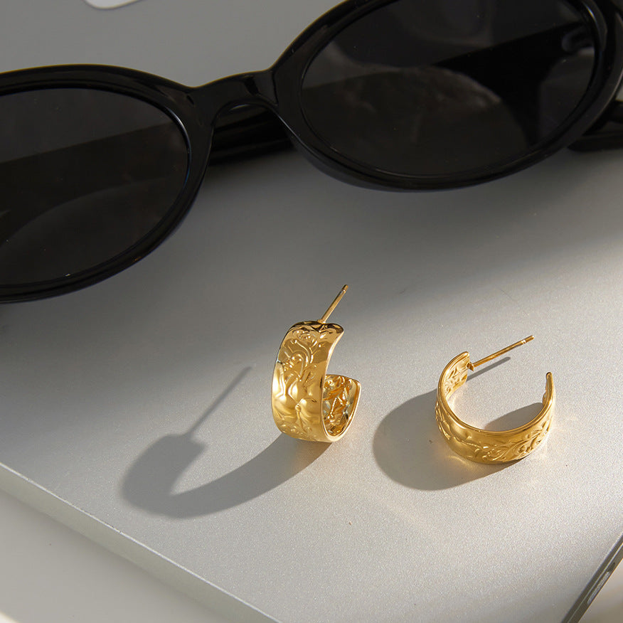 Gold hoop earrings on a white surface with sunglasses and a book.