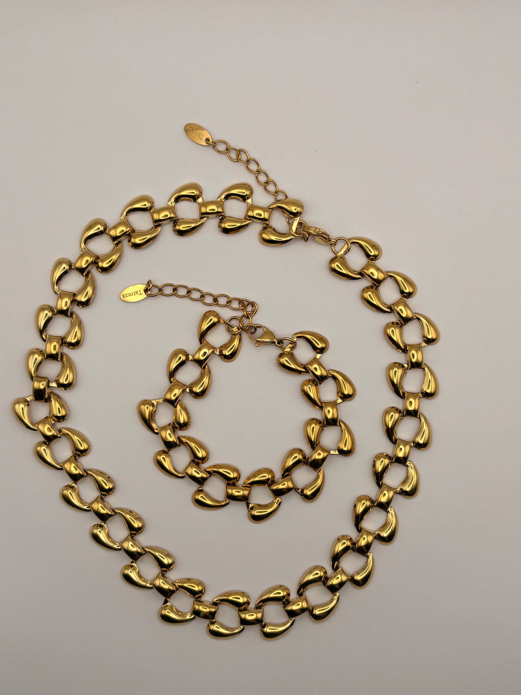 A gold-tone chunky link chain necklace and matching bracelet displayed on a light gray background.