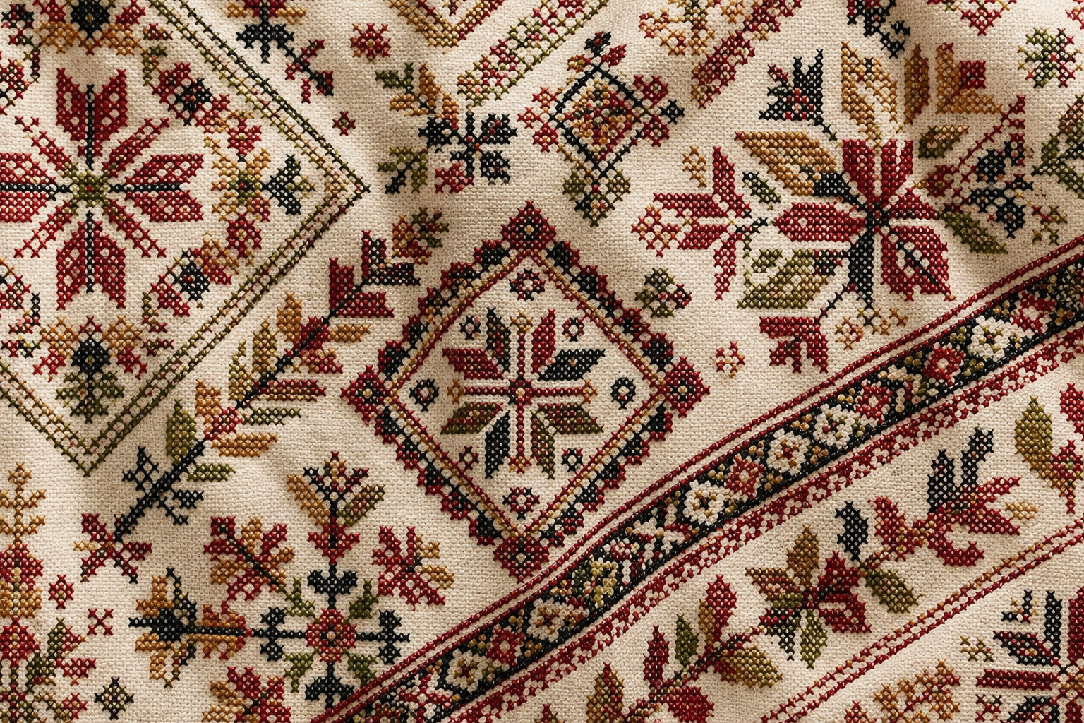 Close-up of a cream-colored embroidered textile with traditional geometric and floral motifs in red, green, brown, and black thread.