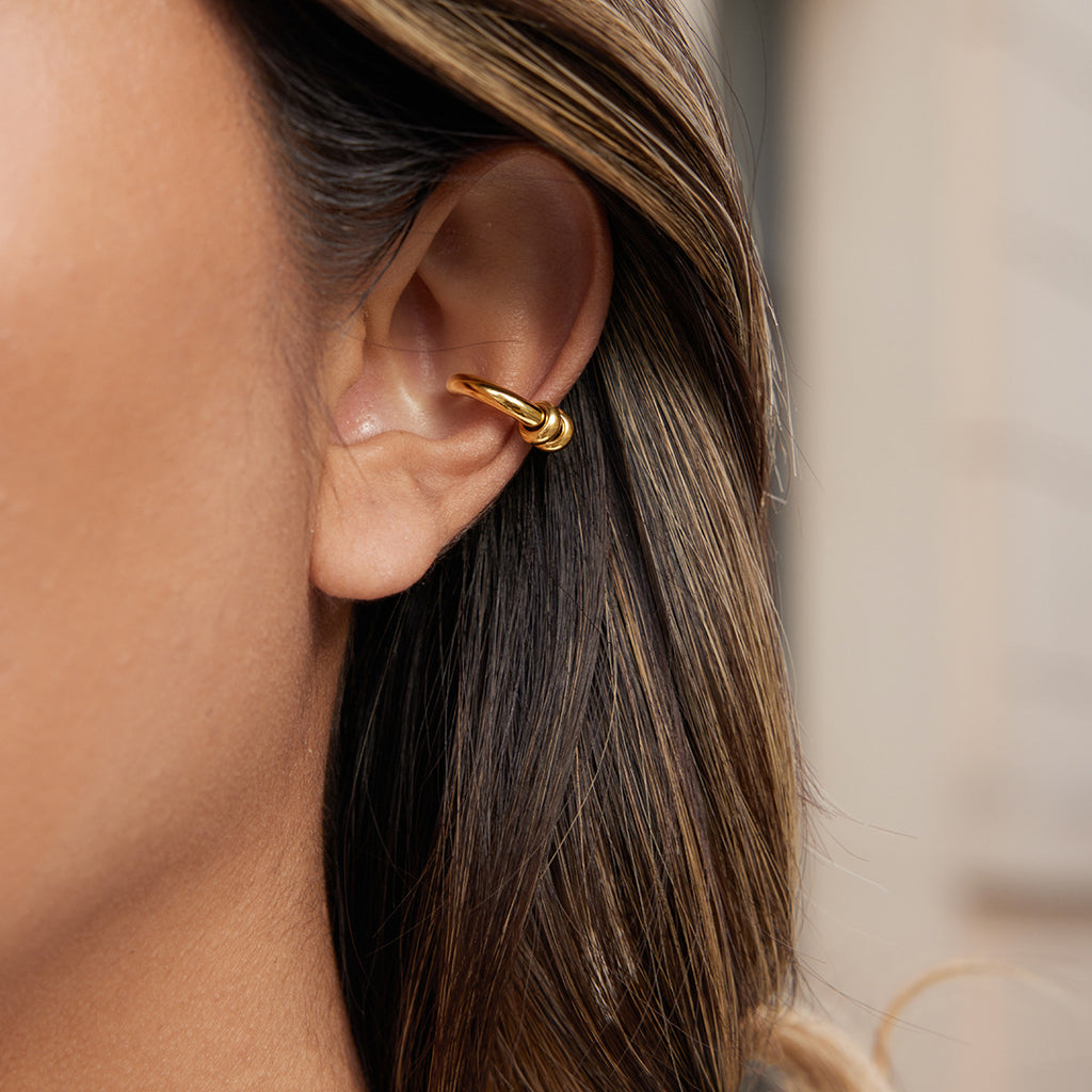 Close-up of a person wearing a gold hoop earring with a blurred background