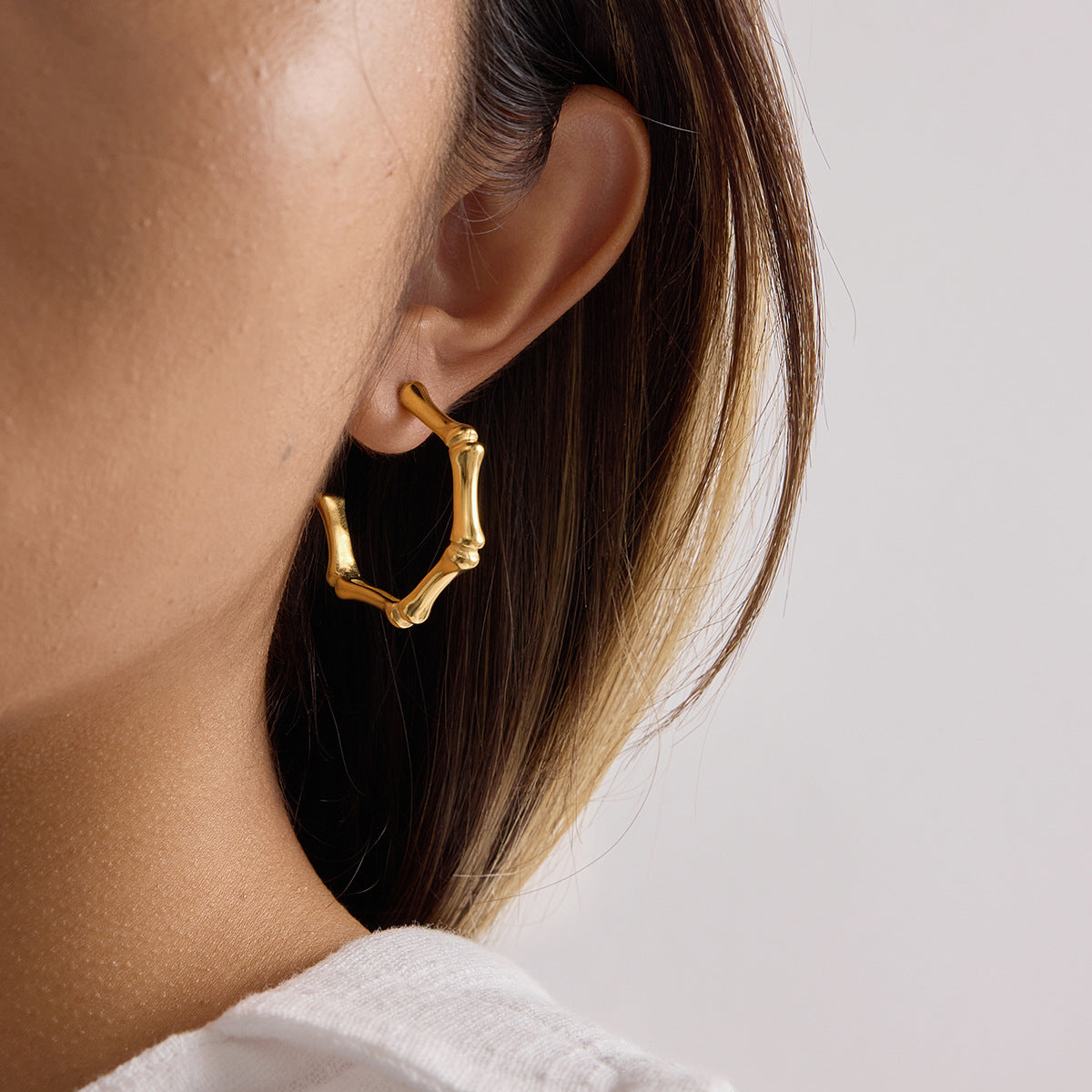 Gold hoop earring worn by a person with a neutral background