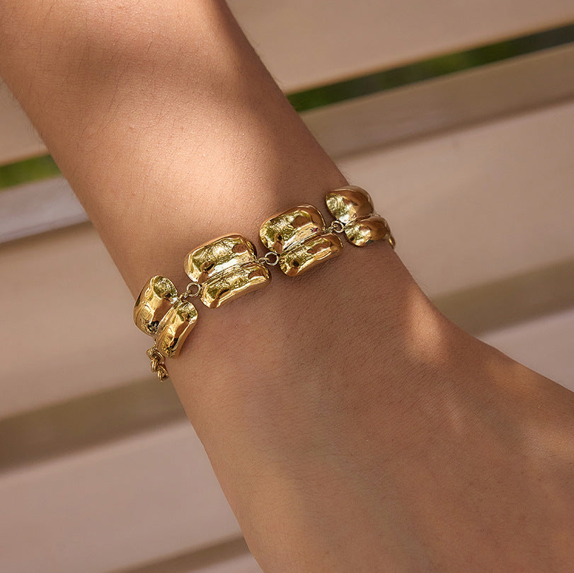 A close-up of a gold bracelet with chunky, organic-shaped links worn on a person's wrist.