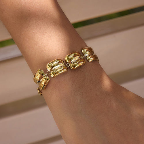A close-up of a gold bracelet with chunky, organic-shaped links worn on a person's wrist.