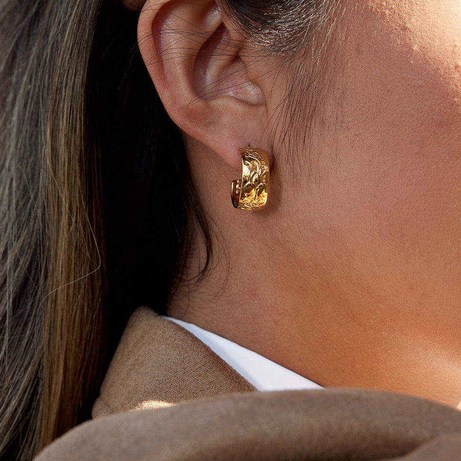 Close-up of a person wearing a gold hoop earring with a neutral background