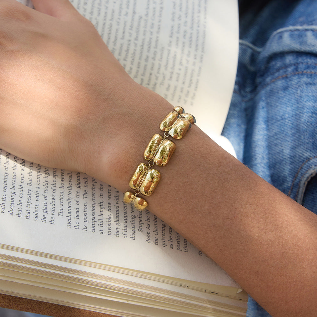 A gold-toned beaded bracelet worn on a person's wrist, resting over an open book with blue denim clothing visible in the background.